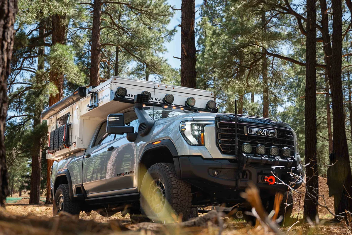 Back Country 6.85 front three-quarter on GMC Sierra HD in pine forest, light bar and roof rack mounted