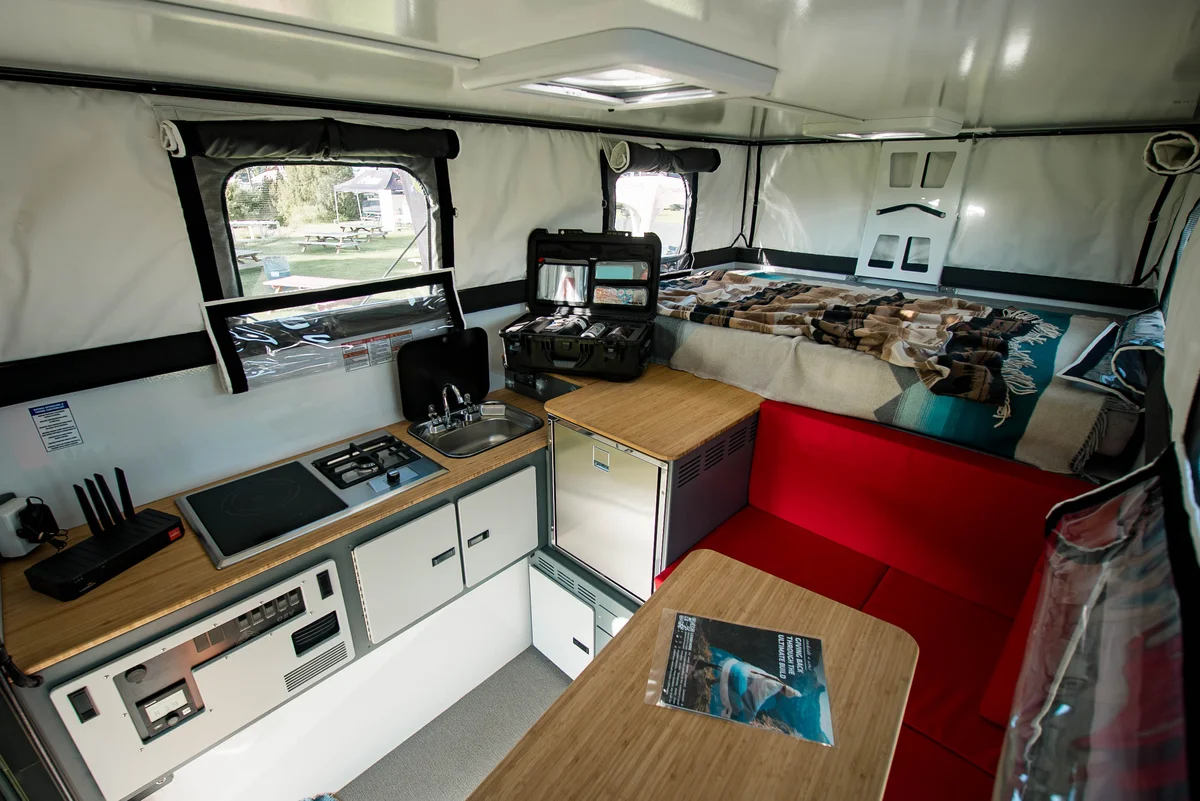 Back Country 6.85 interior showing the galley, compressor fridge, red dinette, bamboo countertops, and queen bed beyond