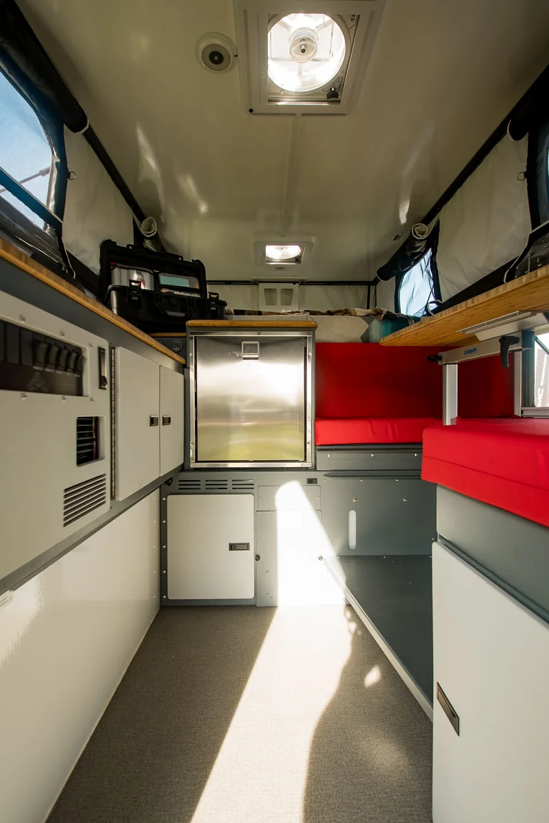 Back Country 6.85 interior lengthwise portrait showing cabinetry, Truma heater, red dinette, and roof vent