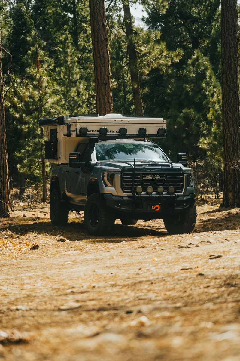 Back Country 6.85 on GMC truck front three-quarter in pine forest, roof closed, light bar and roof rack mounted
