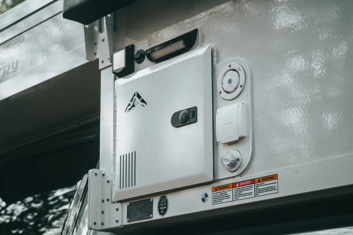 Back Country 6.85 close-up of Truma Aquago hot water heater access panel with OEV mountain badge above