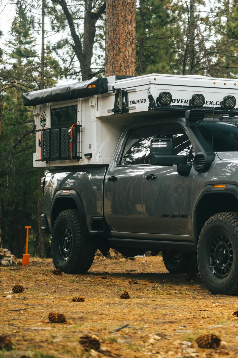 Back Country 6.85 driver side three-quarter with Alu-Cab awning folded, pop-up closed, pine cones on ground