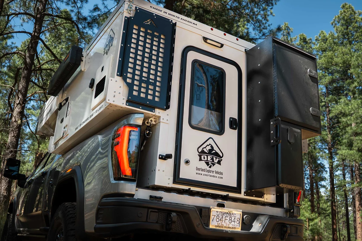 Back Country 6.85 slide-in truck camper, rear three-quarter view with the entry door, MOLLE rack, and storage box, roof deployed