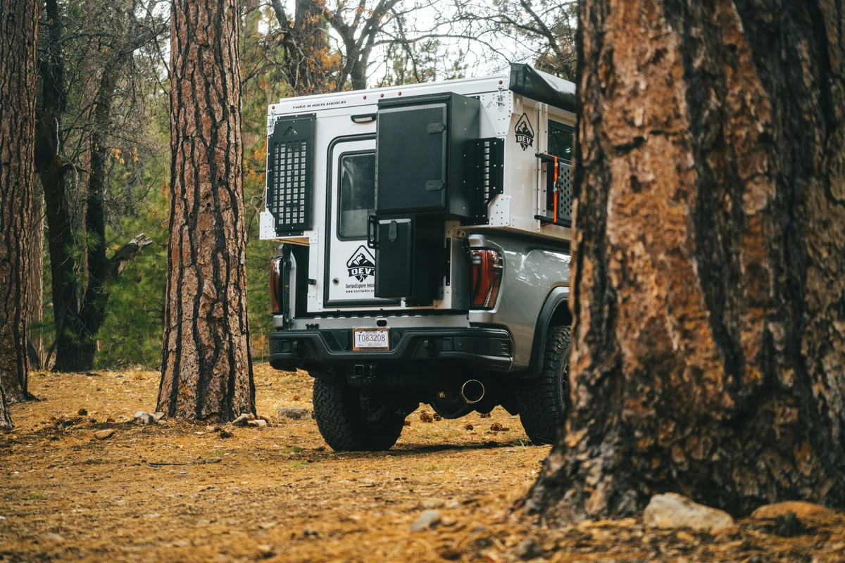 Back Country 6.85 rear view through pine trees with pop-up open, entry door and storage box open