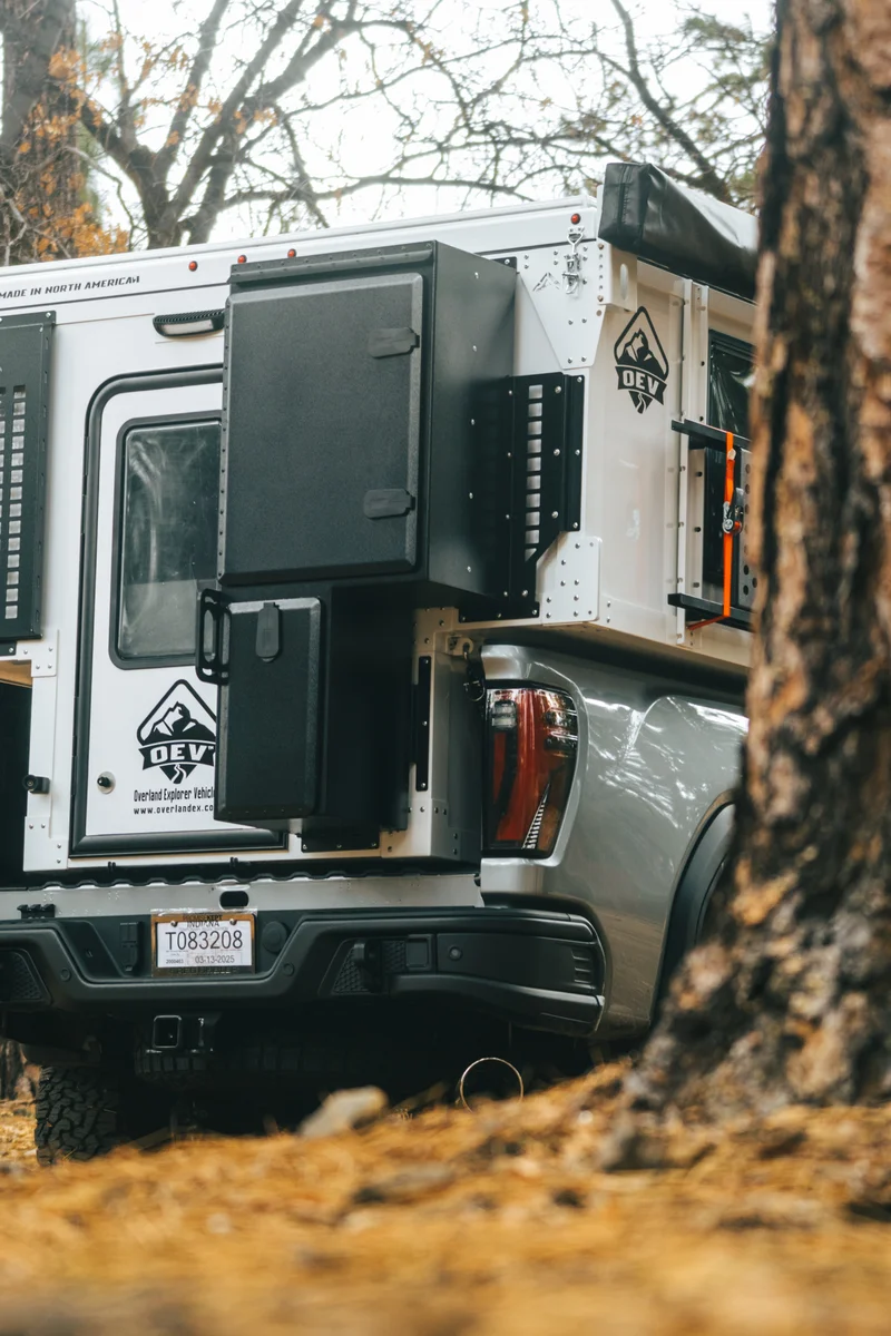 Back Country 6.85 rear close-up portrait through bare trees with entry door open, OEV badge, and storage box