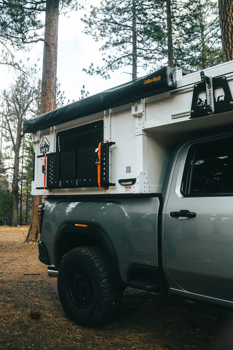 Back Country 6.85 passenger side showing Alu-Cab awning folded, MOLLE panel, and folding steps with orange accents