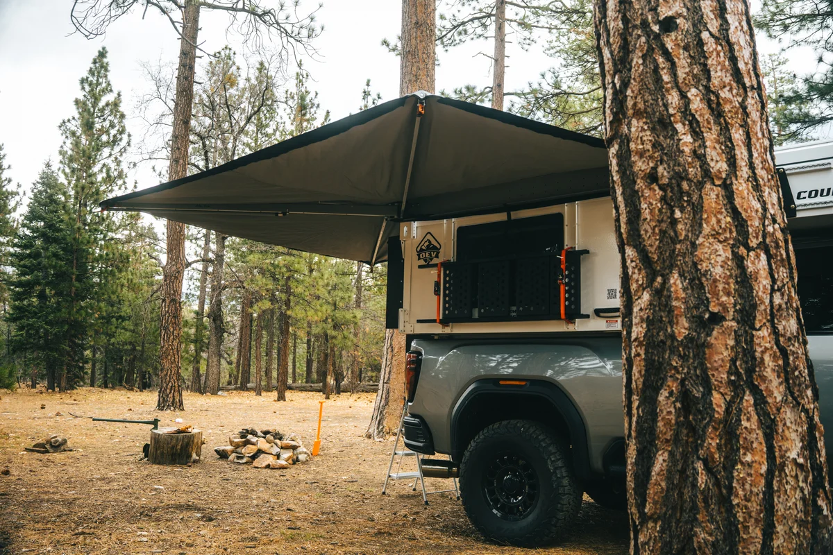 Back Country 6.85 Alu-Cab awning deployed rear three-quarter at basecamp with firewood pile and orange shovel
