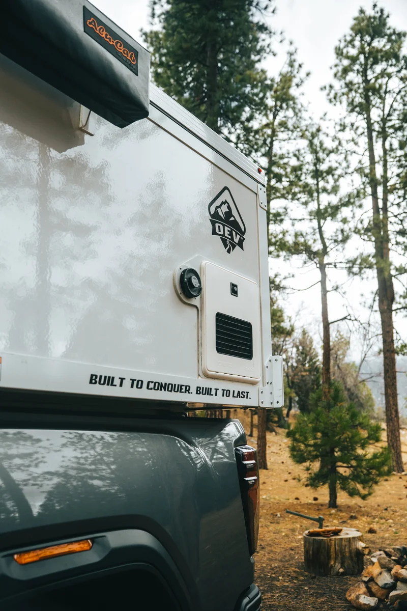 Back Country 6.85 passenger side close-up portrait with OEV badge, Truma heater vent, and 'Built to Conquer' decal