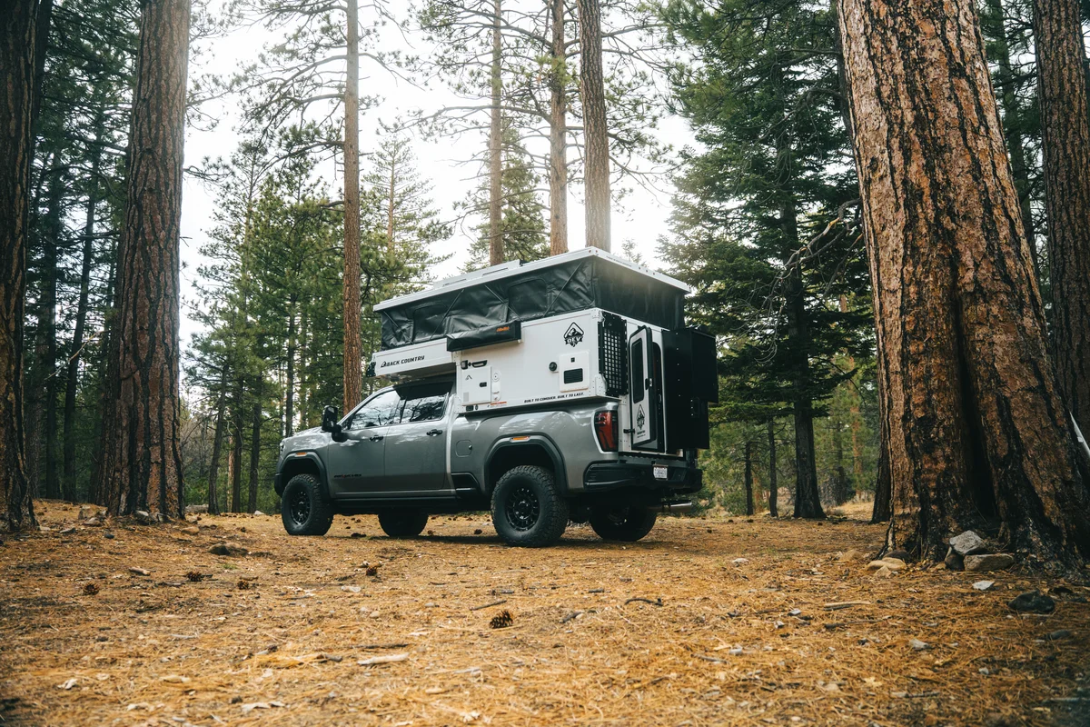 Back Country 6.85 driver-side profile wide landscape in dramatic pine forest light with pop-up roof open