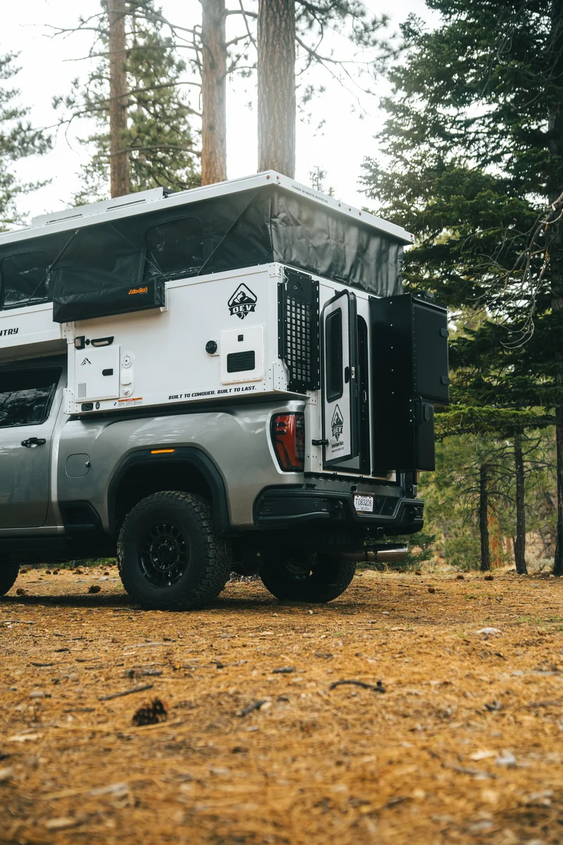 Back Country 6.85 rear three-quarter portrait with pop-up open, entry door open in pine forest