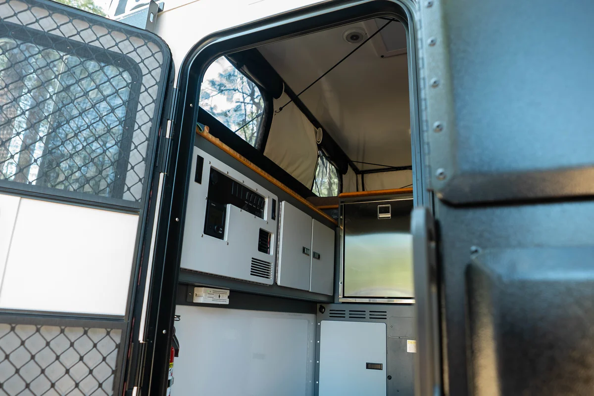 Back Country 6.85 interior view through open screen door showing electrical panel, Truma heater, and cabinetry