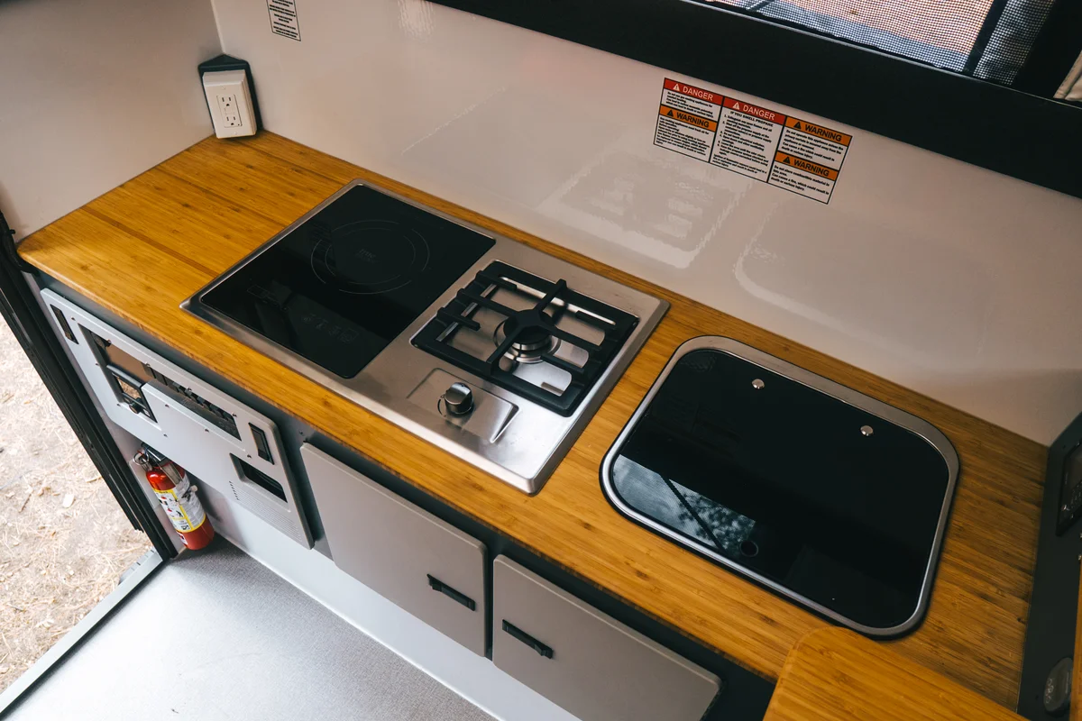 Back Country 6.85 galley overhead showing induction and propane combo cooktop and flush-mount stainless sink with glass cover
