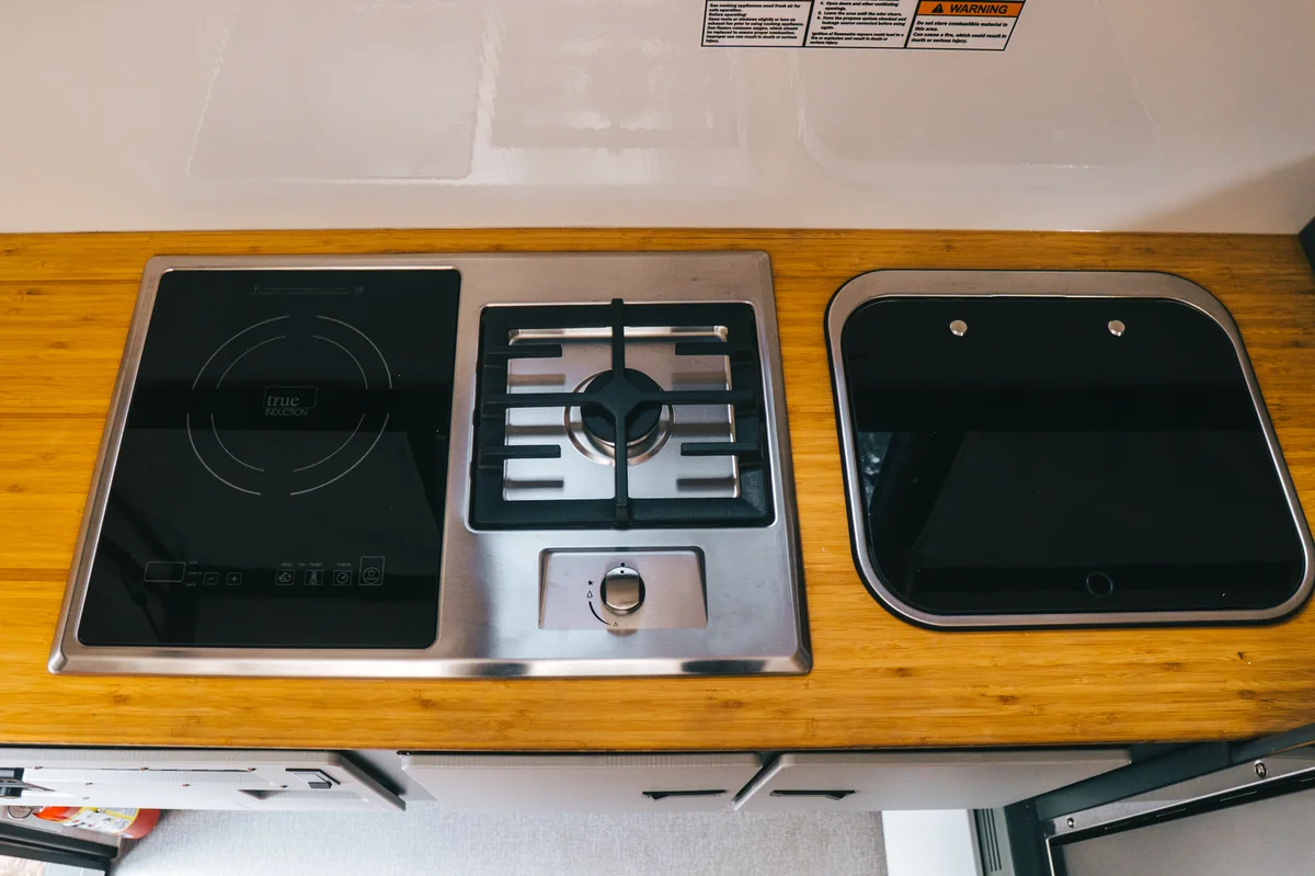 Induction and propane combination cooktop beside a flush-mount stainless sink with glass cover, set into a bamboo countertop in a Back Country 6.85 camper