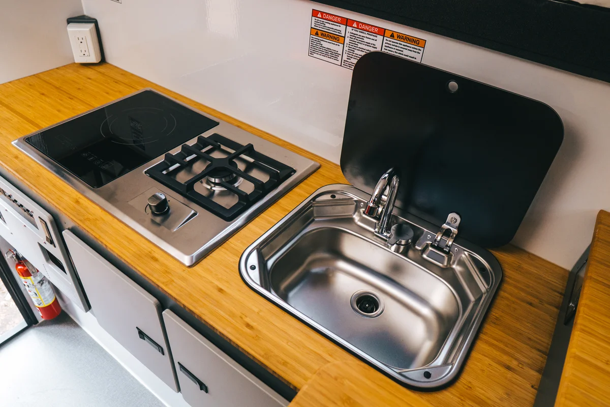Back Country 6.85 galley showing induction and propane cooktop and stainless sink with glass cover open