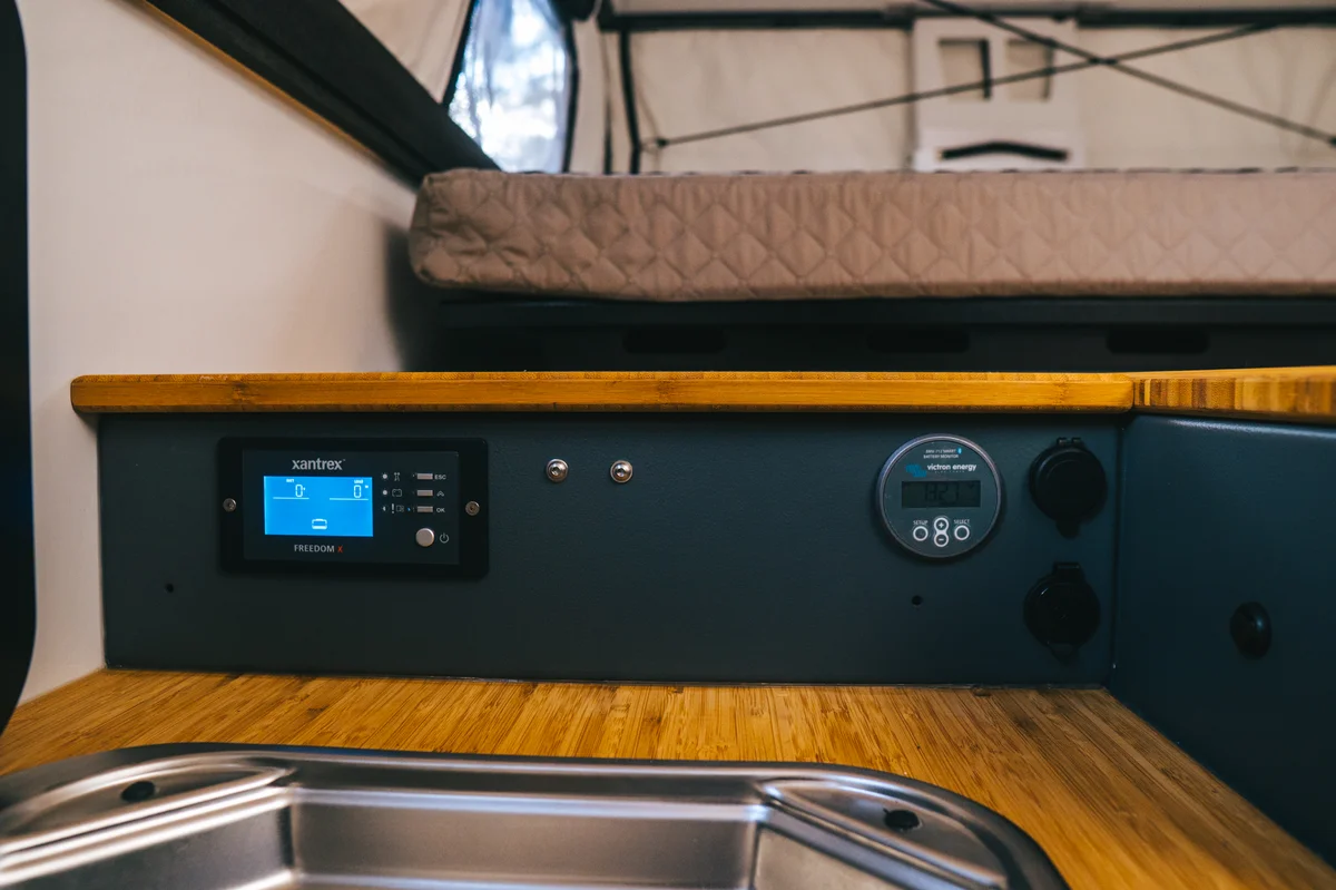 Back Country 6.85 Xantrex inverter and Victron monitor panel with bamboo countertop and queen mattress above