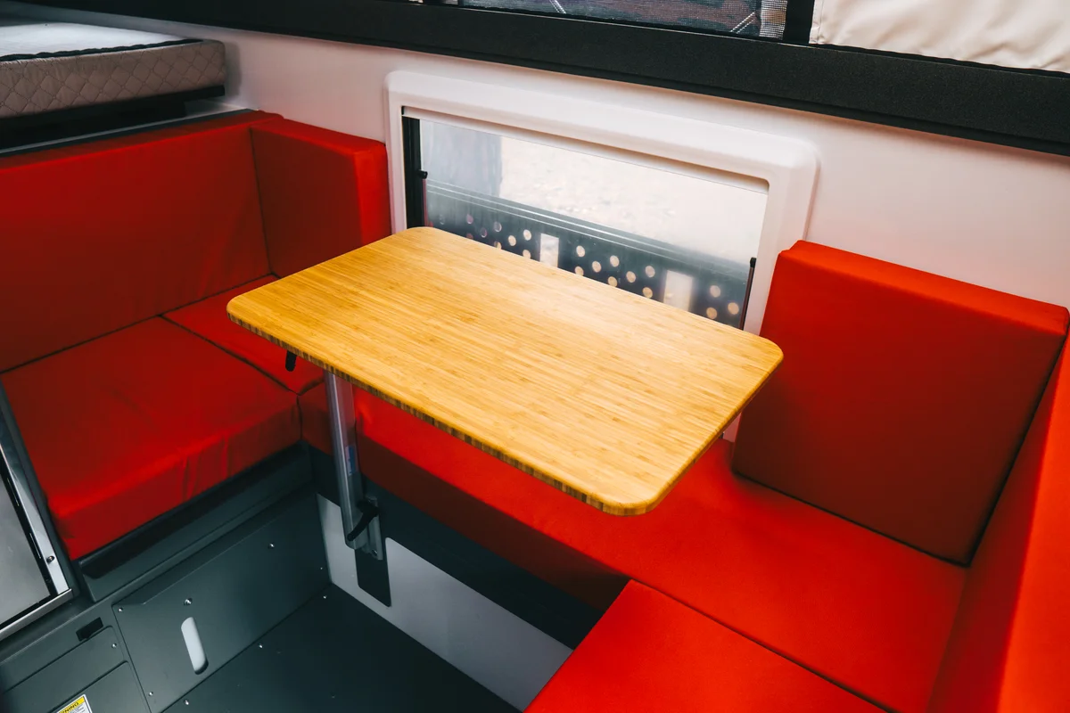 C-shaped red dinette with a bamboo table and the large dual pane acrylic side window behind it, inside a Back Country 6.85 slide-in camper