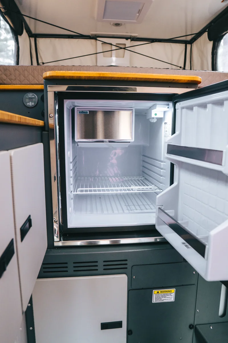 Back Country 6.85 Dometic fridge open wider portrait view with dinette, cabinetry, and bed edge