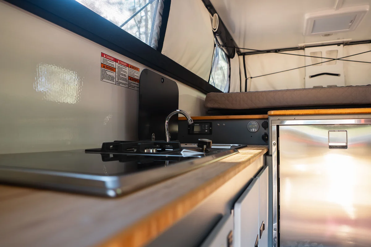 Back Country 6.85 galley detail showing two-burner cooktop, stainless sink with black faucet, and bamboo countertop