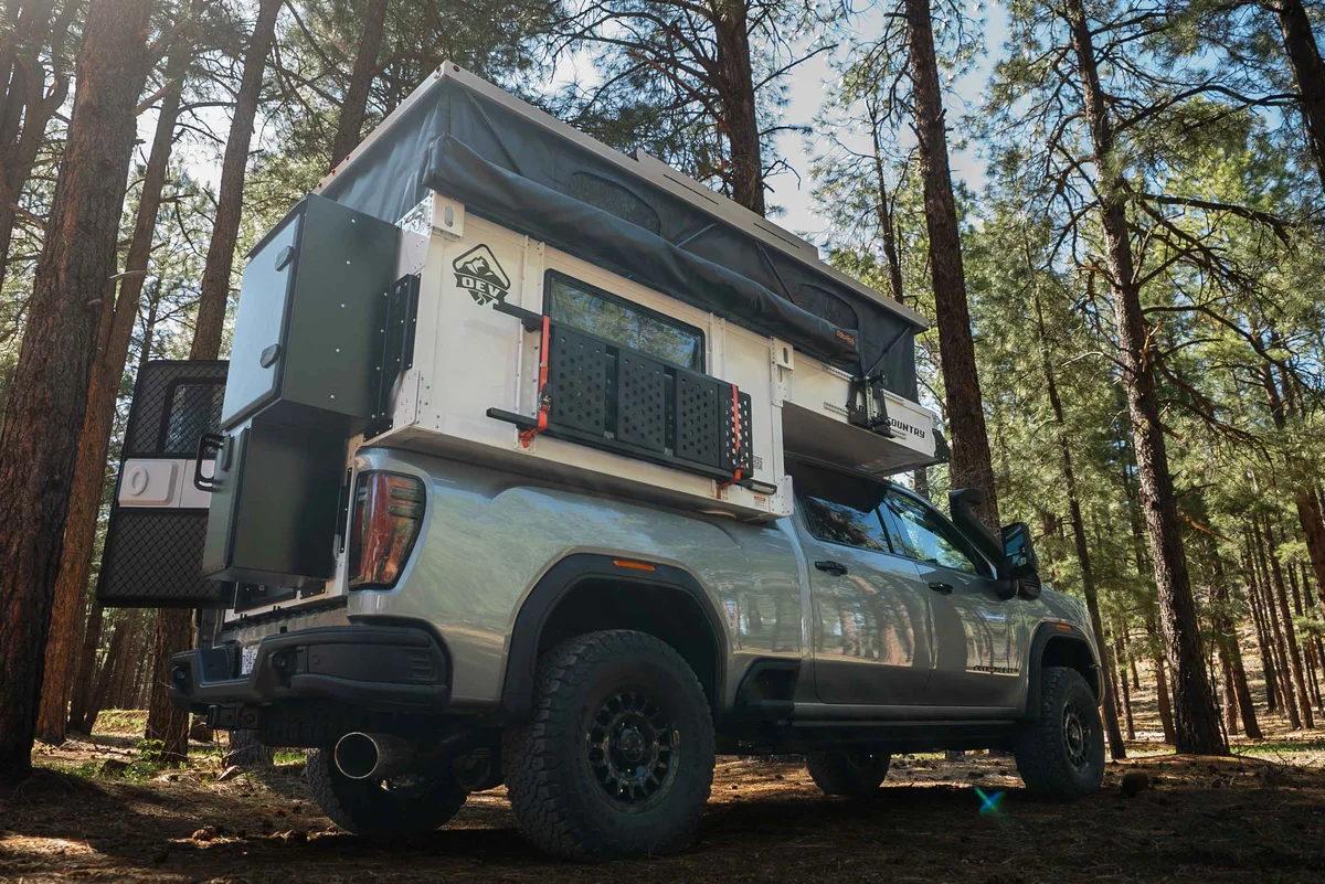 Back Country 6.85 low-angle rear three-quarter with pop-up fully deployed and accessories mounted, pine forest