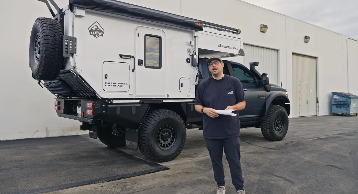 Daniel, founder of Tiny Rig Co., holding the work order beside the OEV Hudson Bay 6.75' camper and Aluma Tray flatbed on the Ram 3500 AEV Prospector XL