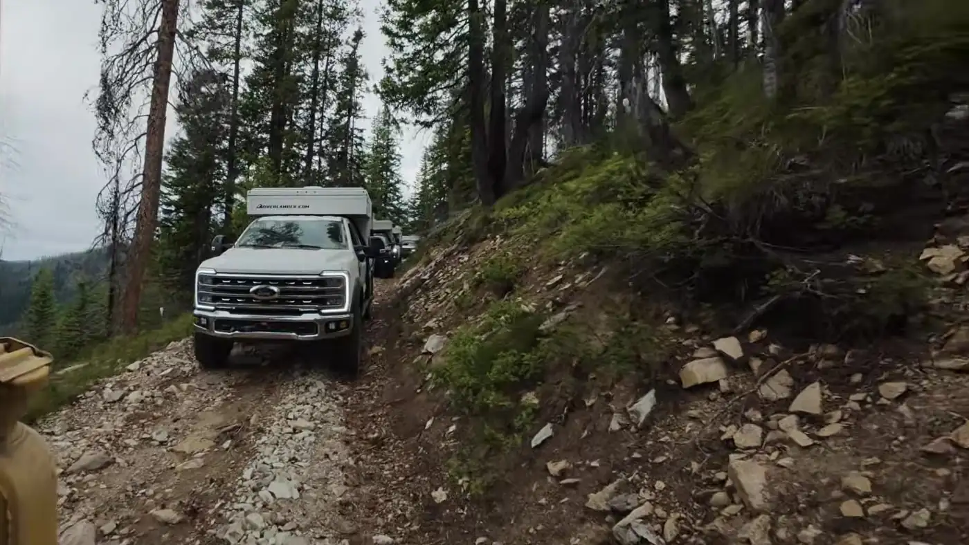 White Ford Super Duty carrying an OEV pop-up camper leads more trucks up a rocky single-lane forest road during the Lolo Motorway leg of Zero Declination's trip